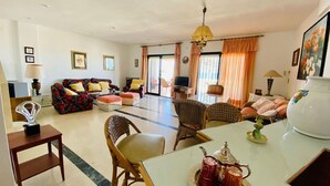 Un salón amplio con un conjunto de sofás, una mesa de comedor con tetera y una televisión.