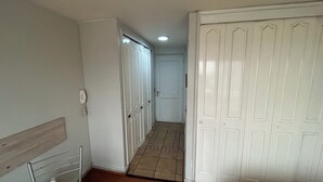 Een smalle gang met witte deuren, een betegelde vloer en een houten bankje aan de linkerkant.