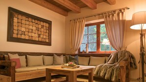 Um quarto aconchegante com um banco de madeira, um sofá, uma mesa com livros e uma janela grande com cortinas.