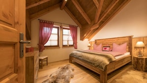 Um quarto aconchegante com teto de madeira, cama com roupa de cama xadrez, tapete de pele e mesa de cabeceira com abajur.