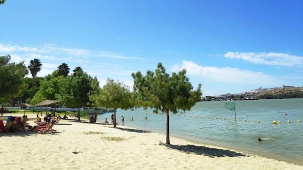 A beach with people sunbathing and swimming, surrounded by trees and a clear sky. - Holiday Home in Andalucia Near Caminito del Rey (Arcos de la Frontera)