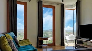A living room with a sofa, a TV, and a view of a cityscape through large windows. - Holiday Home in Andalucia Near Caminito del Rey (Arcos de la Frontera)