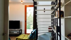 A modern living room with a staircase, a flat-screen TV, and a bookshelf. - Holiday Home in Andalucia Near Caminito del Rey (Arcos de la Frontera)