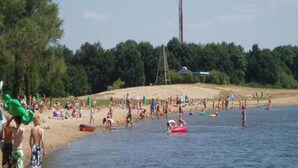 A crowded lakeside beach with people swimming and playing, a sailboat, and a tall structure in the background. - Detached Holiday Home in Nijmegen With Sauna (Ewijk)