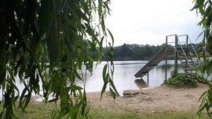 A lakeside view with a metal staircase leading into the water, surrounded by greenery and a grassy area. - Detached Holiday Home in Nijmegen With Sauna (Ewijk)
