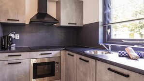A modern kitchen with a built-in oven, a sink, and a window with blinds. - Detached Holiday Home in Nijmegen With Sauna (Ewijk)