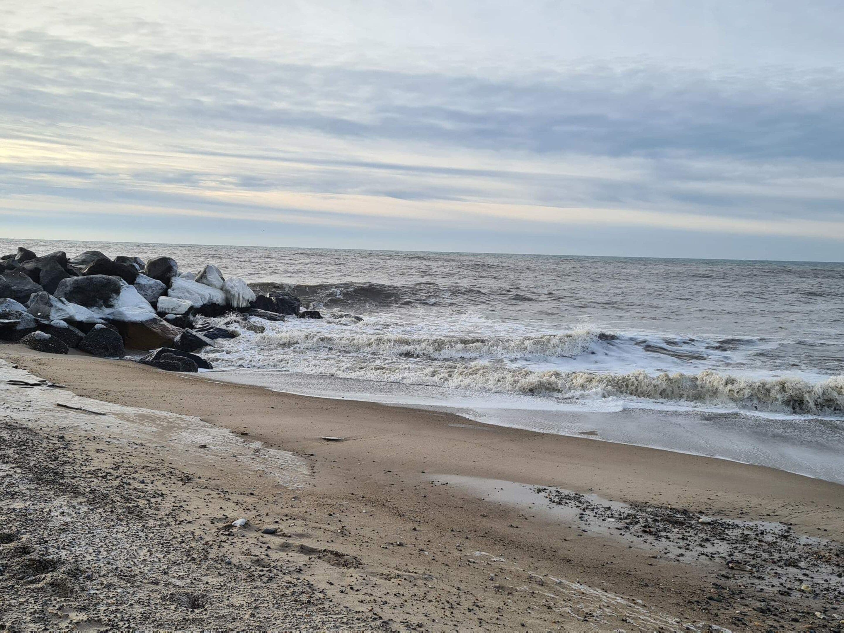 Une plage où les vagues s’écrasent contre les rochers et où s’étend une rive sablonneuse.