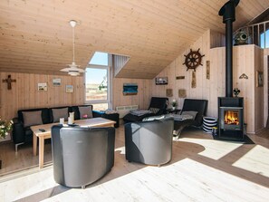 A cozy cabin interior with a wooden ceiling, a fireplace, and a view of the outdoors. - 8 Person Holiday Home in Lemvig (Lemvig)