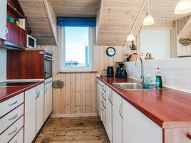 Cocina compacta con armarios de madera, microondas, lavamanos y ventana con vistas.