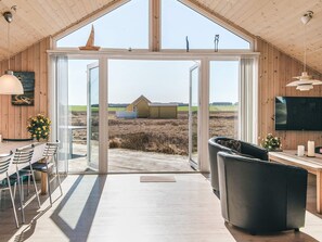 A spacious room with a large sliding glass door leading to an outdoor area, a comfortable seating area with a sofa and chairs, a flat-screen TV mounted on the wall, and a wooden ceiling. - 8 Person Holiday Home in Lemvig (Lemvig)
