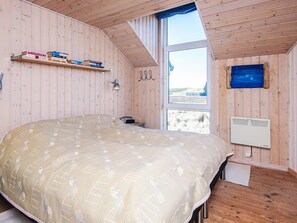 A bedroom with a large bed, a window, a heater, and a shelf with books.