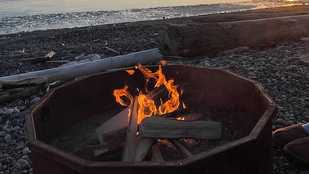 A beach scene with a fire pit in the foreground and a sunset in the background.