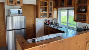 A compact kitchen with wooden cabinets, a stainless steel refrigerator, a microwave, and a sink.