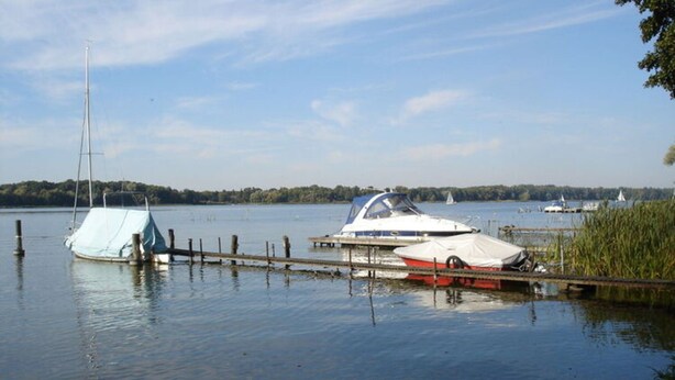 A calm lake with boats docked at a pier, surrounded by trees and clear skies. - Bungalow Oberspreewald 3 (Schwielochsee)