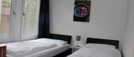 A hotel room with two single beds, a bedside table with a lamp, and a wall-mounted artwork.