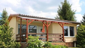 A single-story house with a porch, brick foundation, and a small garden area with various plants. - Bungalow Oberspreewald 3 (Schwielochsee)
