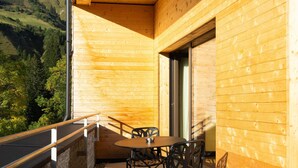 Un balcón de madera con una mesa y sillas, con vista a un paisaje montañoso.