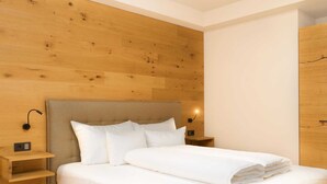 Una cama bien tendida con sábanas blancas en una habitación con paneles de madera en las paredes y una mesita de noche sencilla con una lámpara.