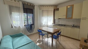 A compact kitchen with a dining table and chairs, a sofa, and a kitchenette. - Solaris by Interhome (Rosolina Mare)