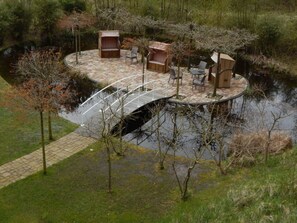 A circular outdoor seating area with a wooden bench and chairs, a small table, and a bridge over a water body.