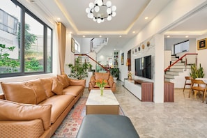 A modern living room with a leather sofa, a coffee table, and a TV. There is a staircase leading to another level.