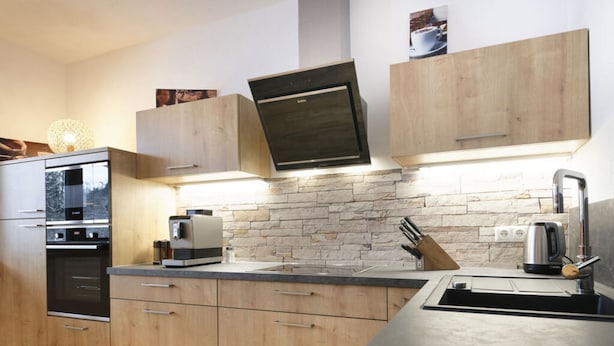 Una cocina moderna con armarios de madera, horno empotrado, cafetera y salpicadero de piedra.