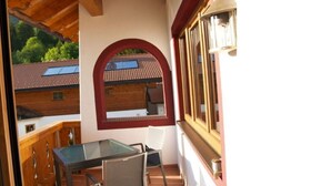 Un balcón con mesa y sillas de vidrio, techo de madera y vistas a edificios cercanos.