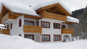 Una chaleta de varios pisos con balcones de madera y tejados cubiertos de nieve, en un paisaje nevado.