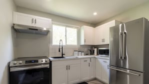 A modern kitchen with white cabinets, stainless steel appliances, and a large window.