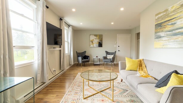 A modern living room with a sofa, armchairs, a glass coffee table, and a TV.