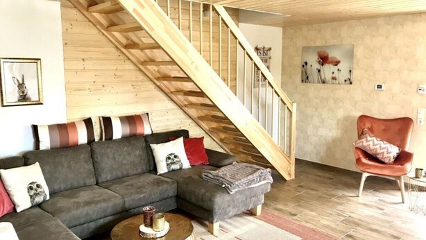 A living room with a wooden staircase, grey sofa, and a red armchair. - Holiday Home Goldstuck (Oberharz am Brocken)