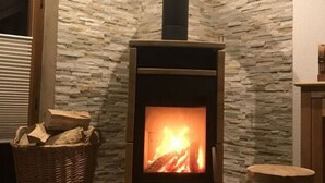A wood-burning stove in a corner with a stone wall, a wicker basket with firewood, and a wooden stool. - Holiday Home Goldstuck (Oberharz am Brocken)