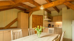 A spacious kitchen with wooden beams, a dining table with chairs, and a vase of flowers. - Eindverdieping DG (Sebnitz)