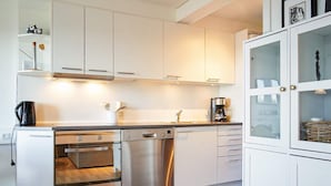 Une cuisine moderne avec des meubles blancs, un lave-vaisselle Bosch, un four et une machine à café.