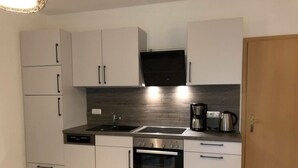 A compact kitchen with white cabinets, a black oven, a stainless steel sink, and a coffee maker. - Beachkeeper Comfortable Holiday Residence (Zingst)