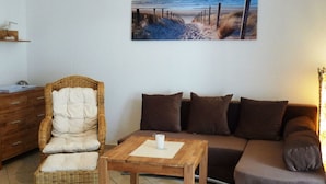A living room with a wicker chair, a wooden coffee table, a brown sofa, and a painting of a beach scene. - Beachkeeper Comfortable Holiday Residence (Zingst)