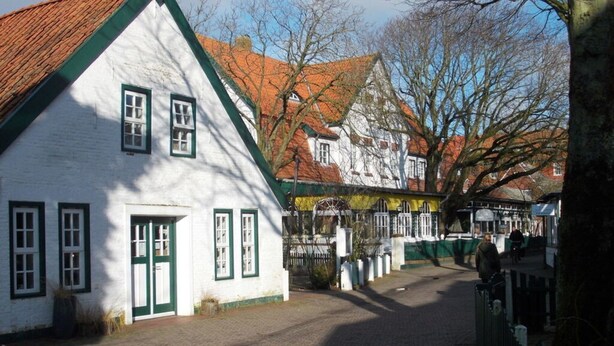 Een traditioneel wit gebouw met groene details en een schuin dak, gelegen aan een geplaveide straat.