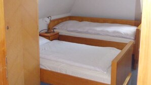 Een kleine, eenvoudige kamer met twee houten stapelbedden, een bureau met lamp en een plafondlamp.
