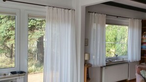 Een kamer met een houten vloer, witte wanden, een radiator, een boekenplank en een raam met witte gordijnen.