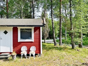 A small red cabin with a white door and window, two white chairs outside, surrounded by trees. - 5 Person Holiday Home in Djurhamn (Djurhamn)
