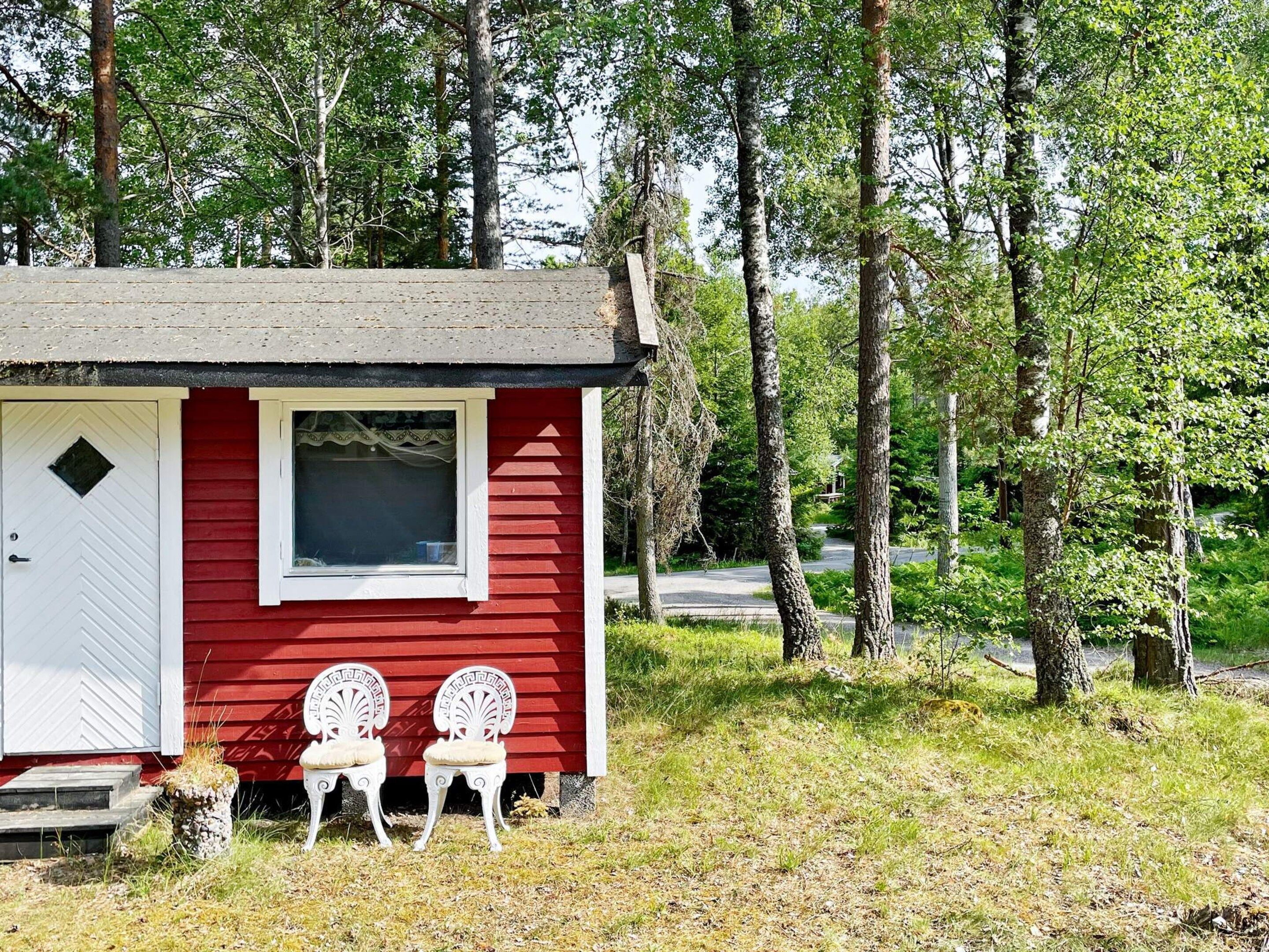A small red cabin with a white door, a window, and two white chairs outside.