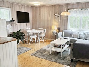 A cozy living room with a dining table and chairs, a sofa, a flat-screen TV, and a large window with curtains. - 5 Person Holiday Home in Djurhamn (Djurhamn)