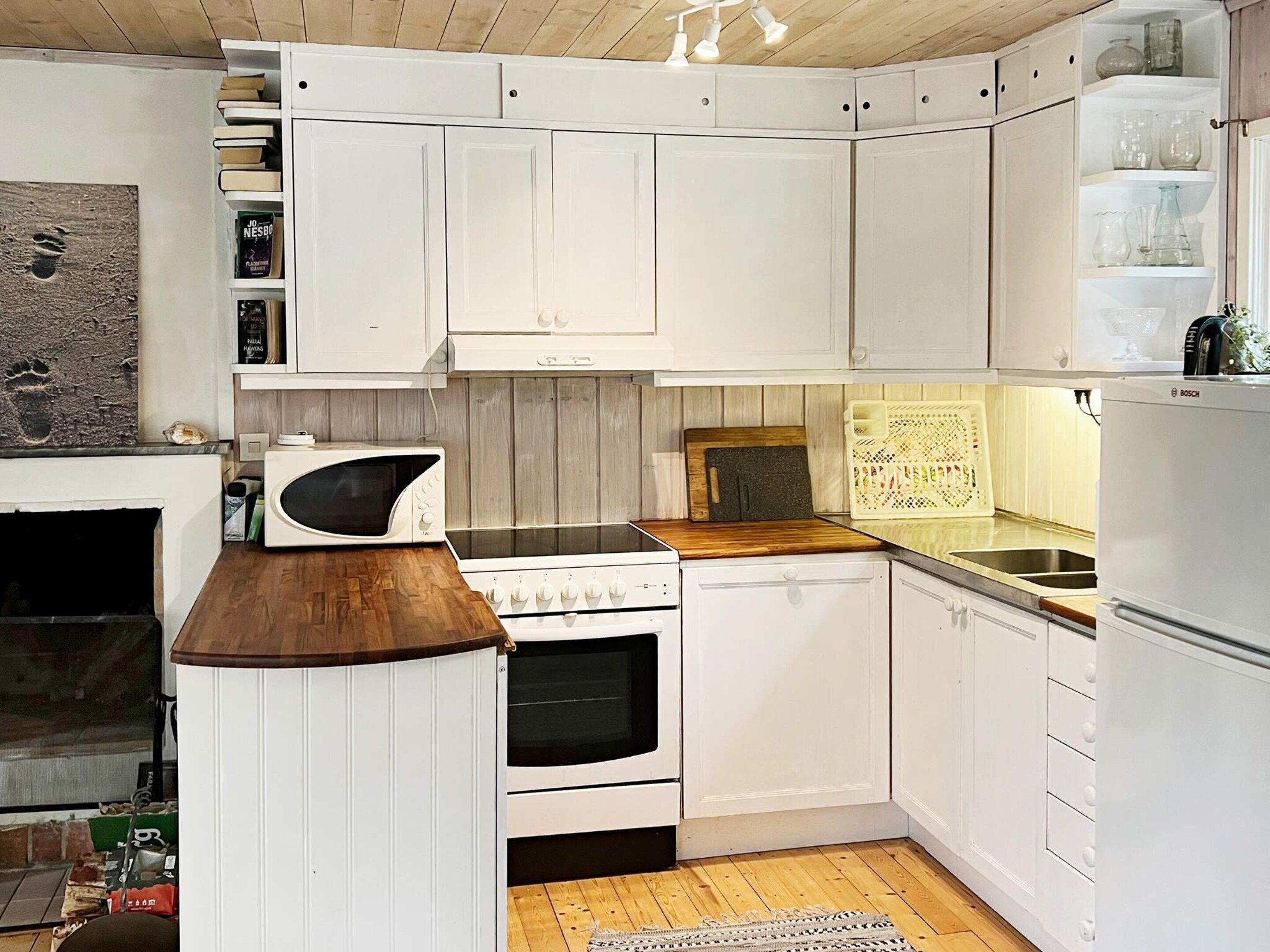 Eine Küche mit weißen Schränken, einer Mikrowelle, einem Backofen und einem Bosch-Kühlschrank.