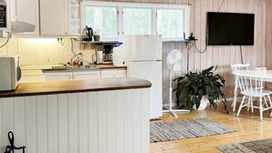 A kitchen with a wooden countertop, white cabinets, a Bosch refrigerator, and a Bosch coffee maker. There is a dining area with a white table and chairs, a white fan, and a potted plant. - 5 Person Holiday Home in Djurhamn (Djurhamn)