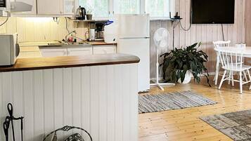 A kitchen with a wooden countertop, white cabinets, a Bosch refrigerator, and a Bosch coffee maker. There is a dining area with a white table and chairs, a white fan, and a potted plant.