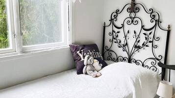 A bedroom with a single bed, a window with lace curtains, a decorative metal headboard, and a bedside lamp.