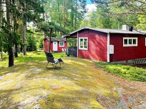 A red cabin with a porch and a single chair, surrounded by a forested area. - 5 Person Holiday Home in Djurhamn (Djurhamn)