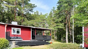 A red cabin with a porch, surrounded by trees. - 5 Person Holiday Home in Djurhamn (Djurhamn)