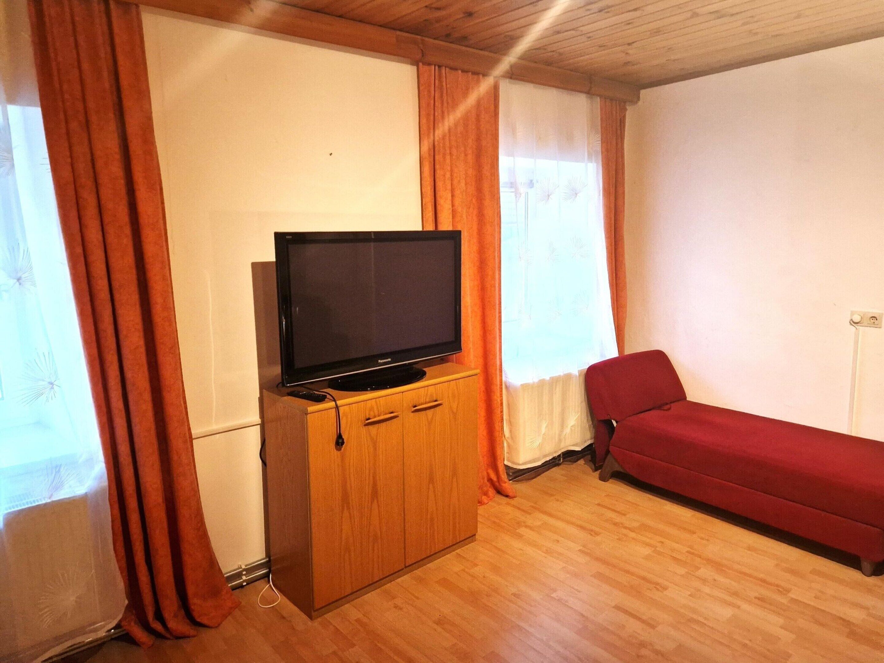 A living room with a television on a wooden cabinet, a red sofa, and a window with curtains.