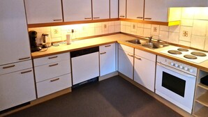 Een compacte keuken met witte kasten, een inbouwvaatwasser, een fornuis en een spoelbak.